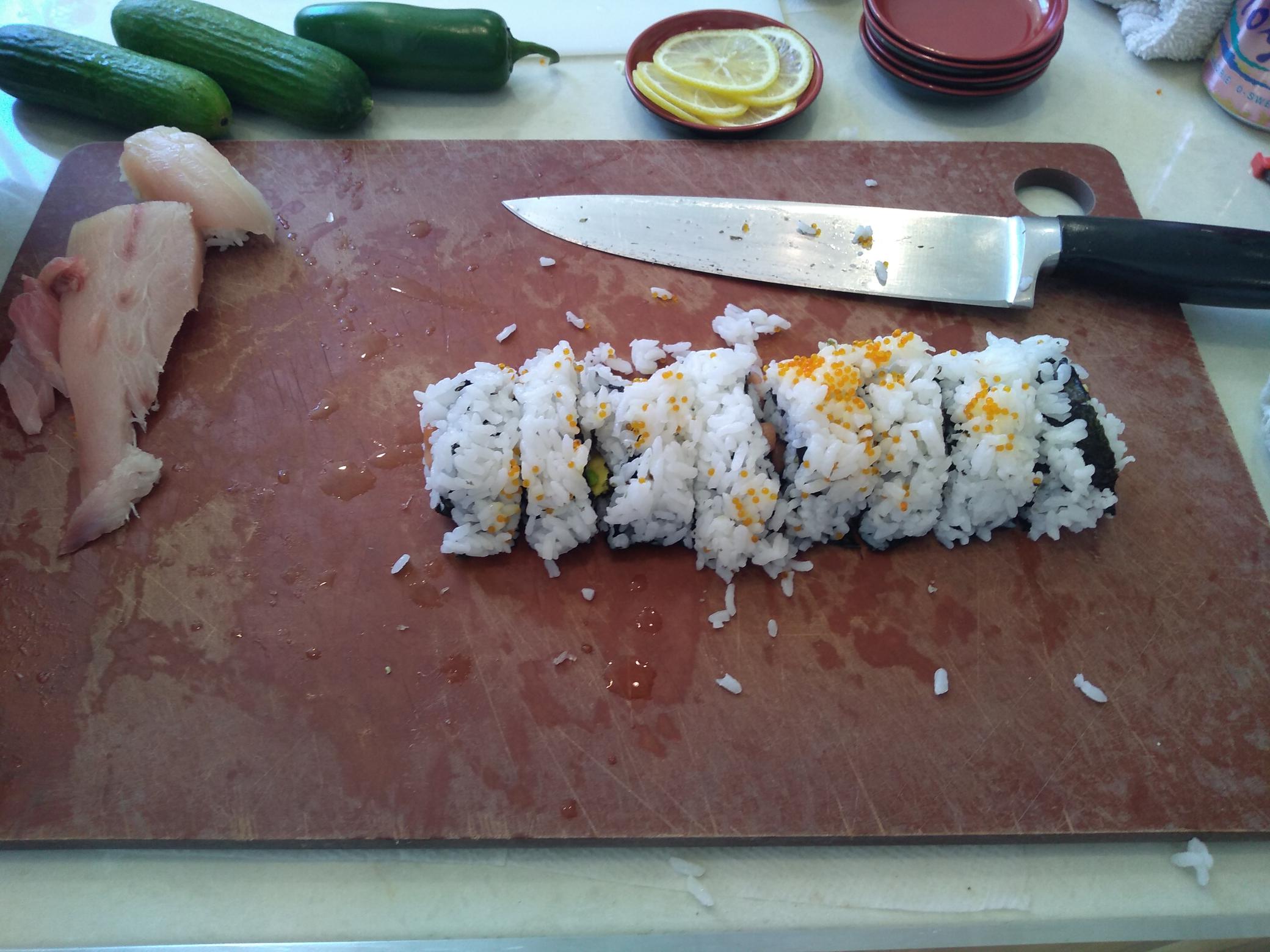 A slightly misshapen log of rice and seaweed, perched proudly on a cutting board with some ingredients scattered artfully about.