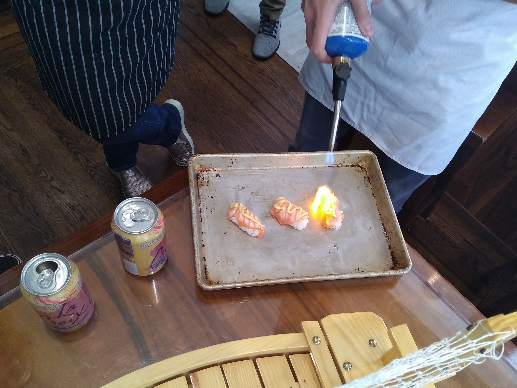 Lit blowtorch being played over a piece of nigiri on a tray.