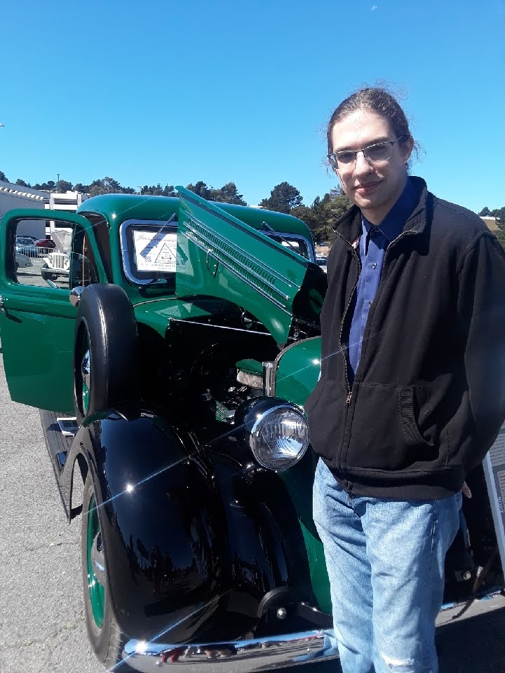Wolf in front of the old green pickup truck, squinting slightly into the sun.