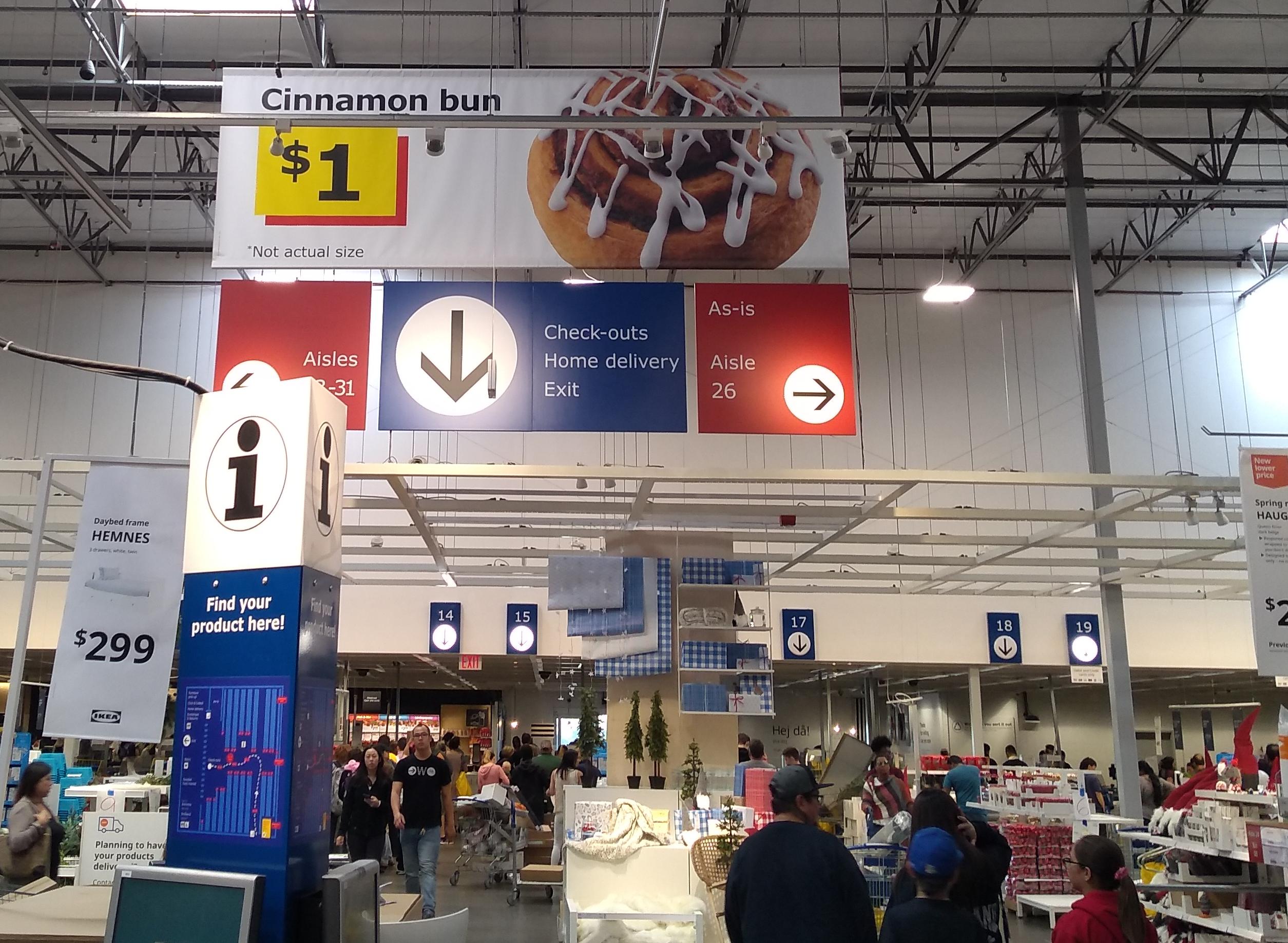 An enormous banner advertising “Cinnamon bun $1”, with a six-foot-tall photograph of the comestible in question and some fine print stating “*Not actual size”
