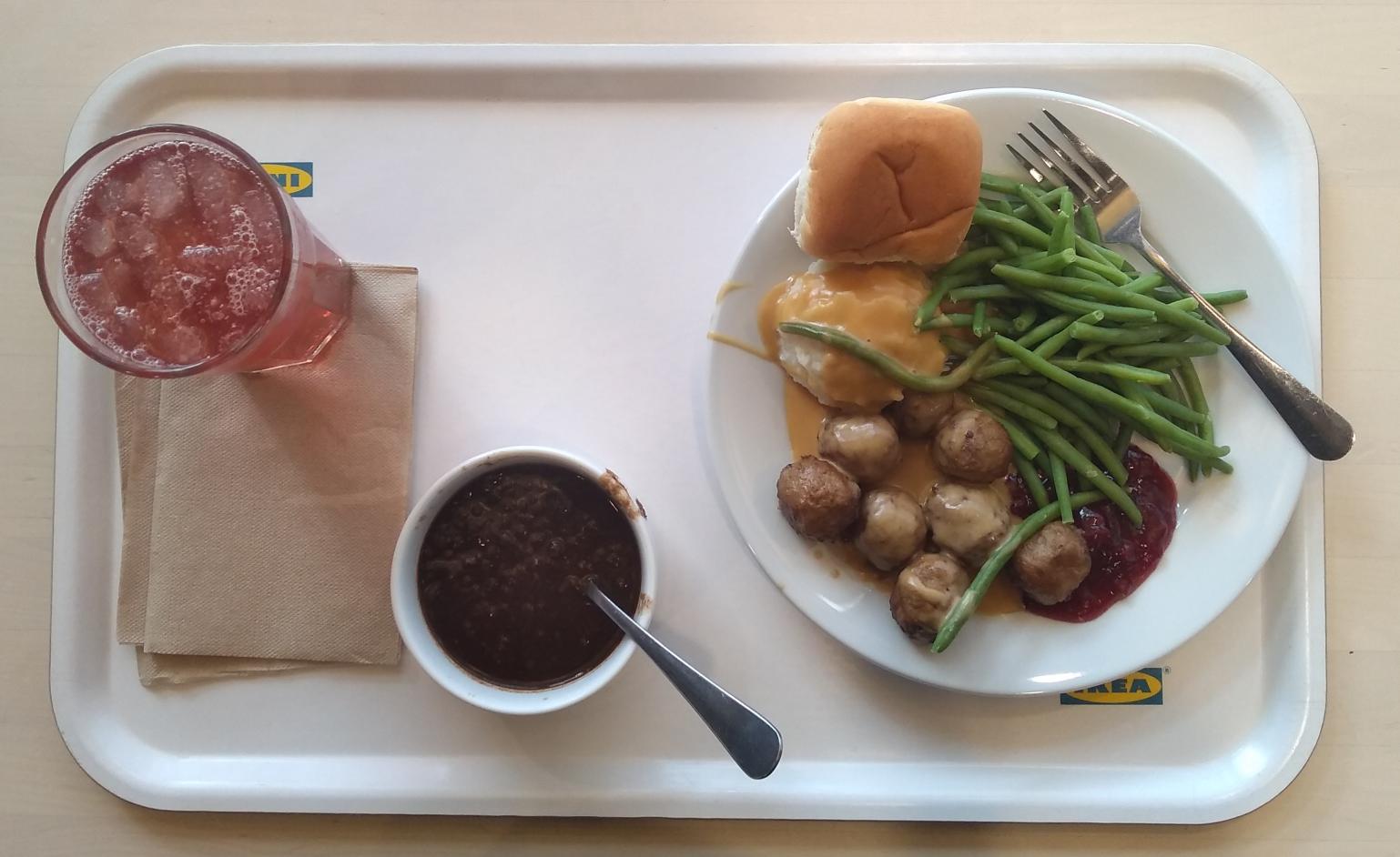 An IKEA-branded cafeteria tray, artfully arranged with a plate of Swedish meatballs, green beans, mashed potatoes, and gravy, plus a bowl of soup, a glass of lingonberry drink, and some paper napkins.