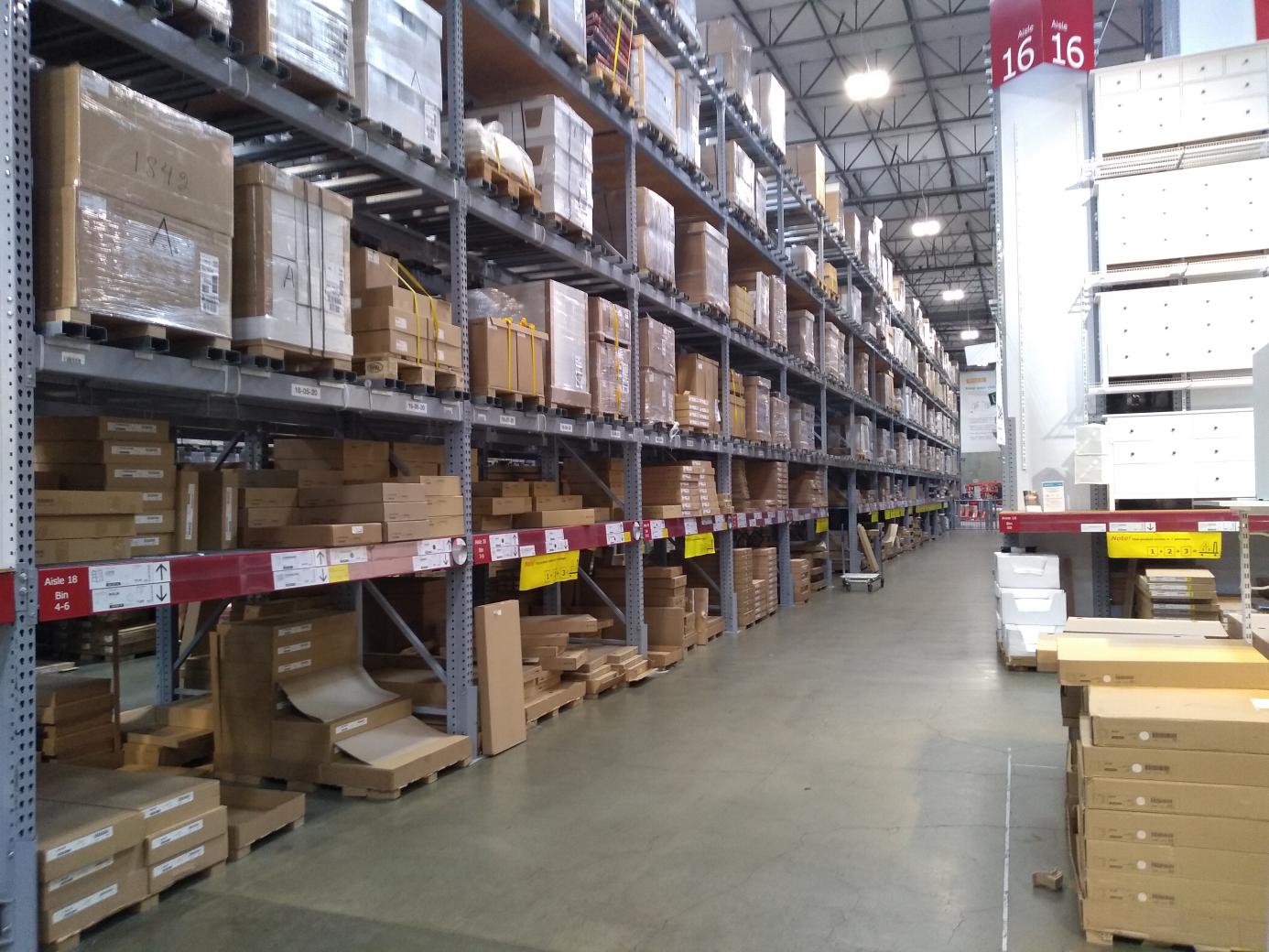 A very long aisle of industrial shelving, with lots of pallets and cardboard boxes.