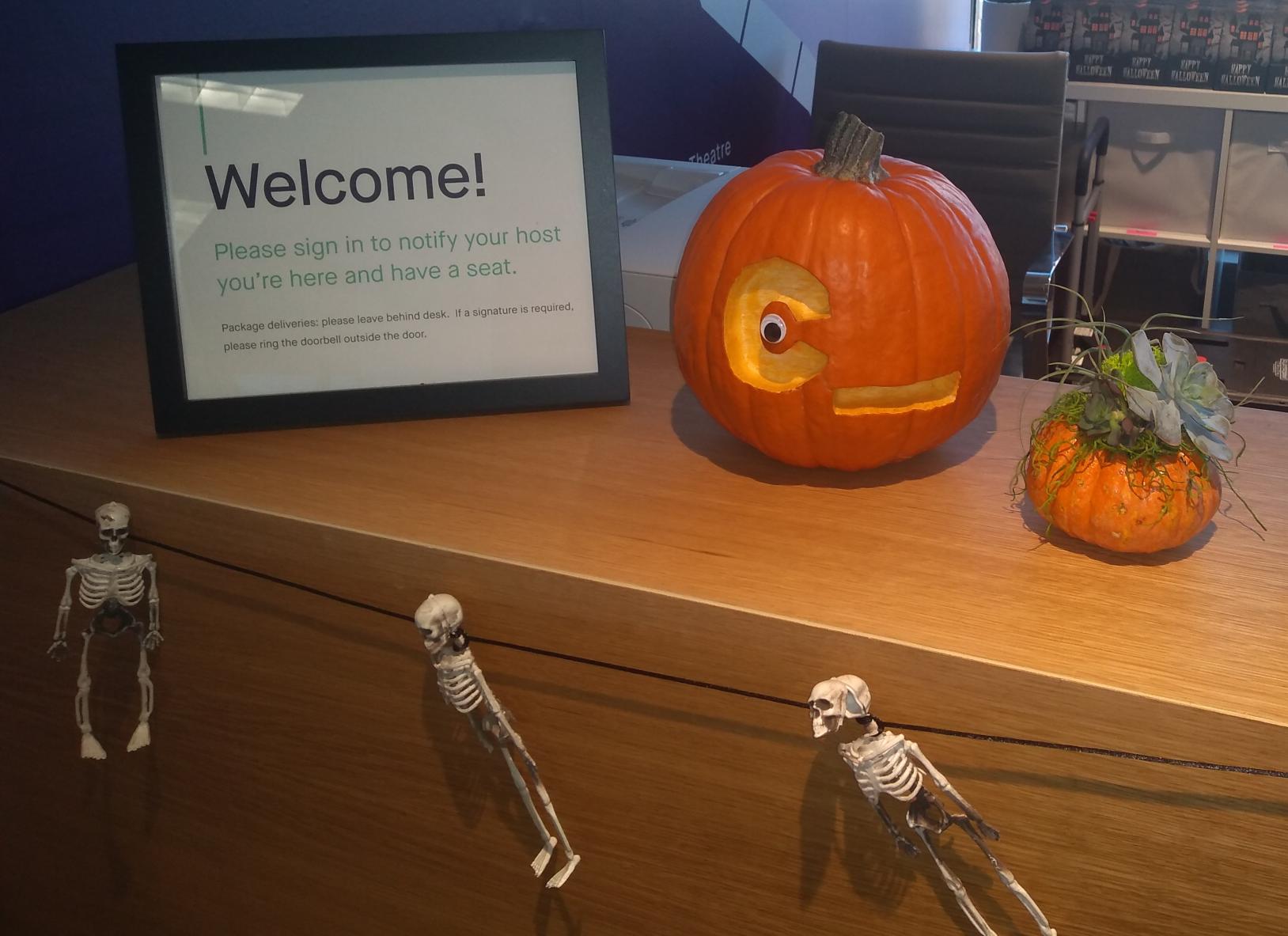 Next to a sign welcoming visitors, a pumpkin with the ‘C_’ logo, with a googly eye in the center of the C.