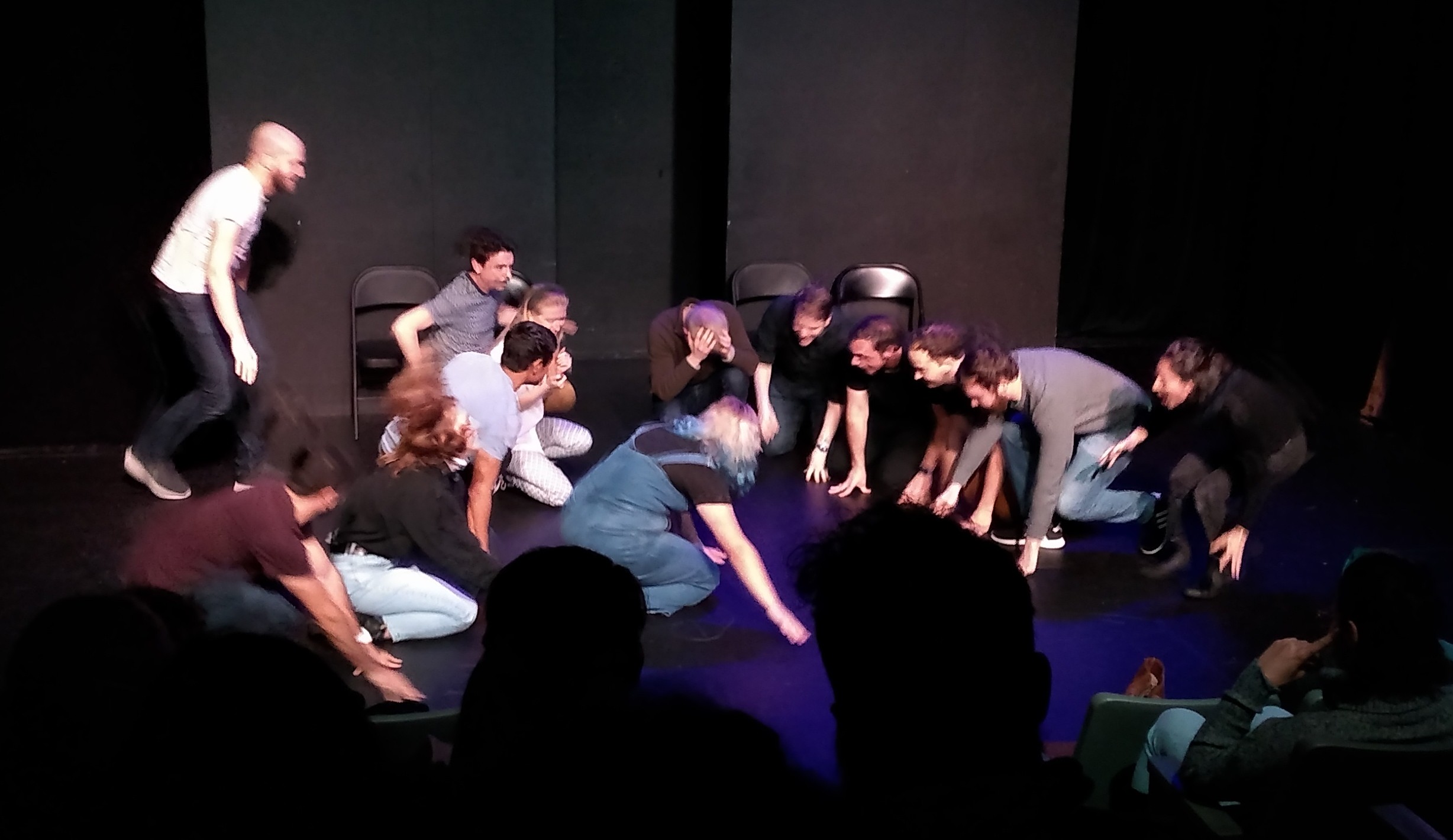 A group of people on stage, crouching down and effecting various silly poses.
