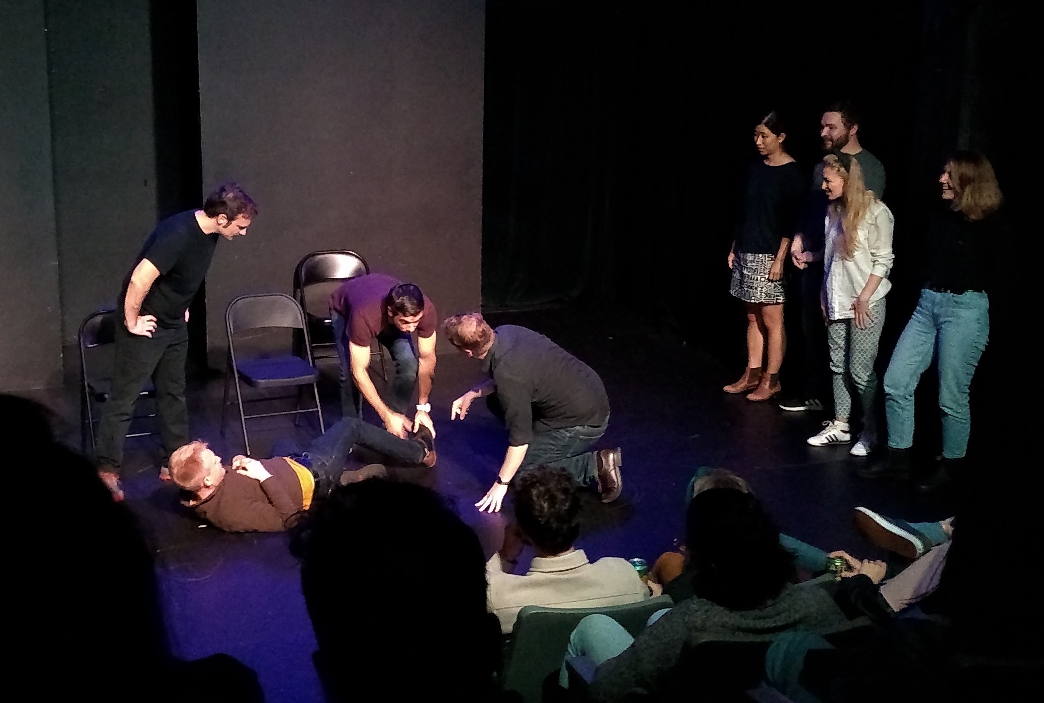 A group of people standing around looking at someone lying on the floor.