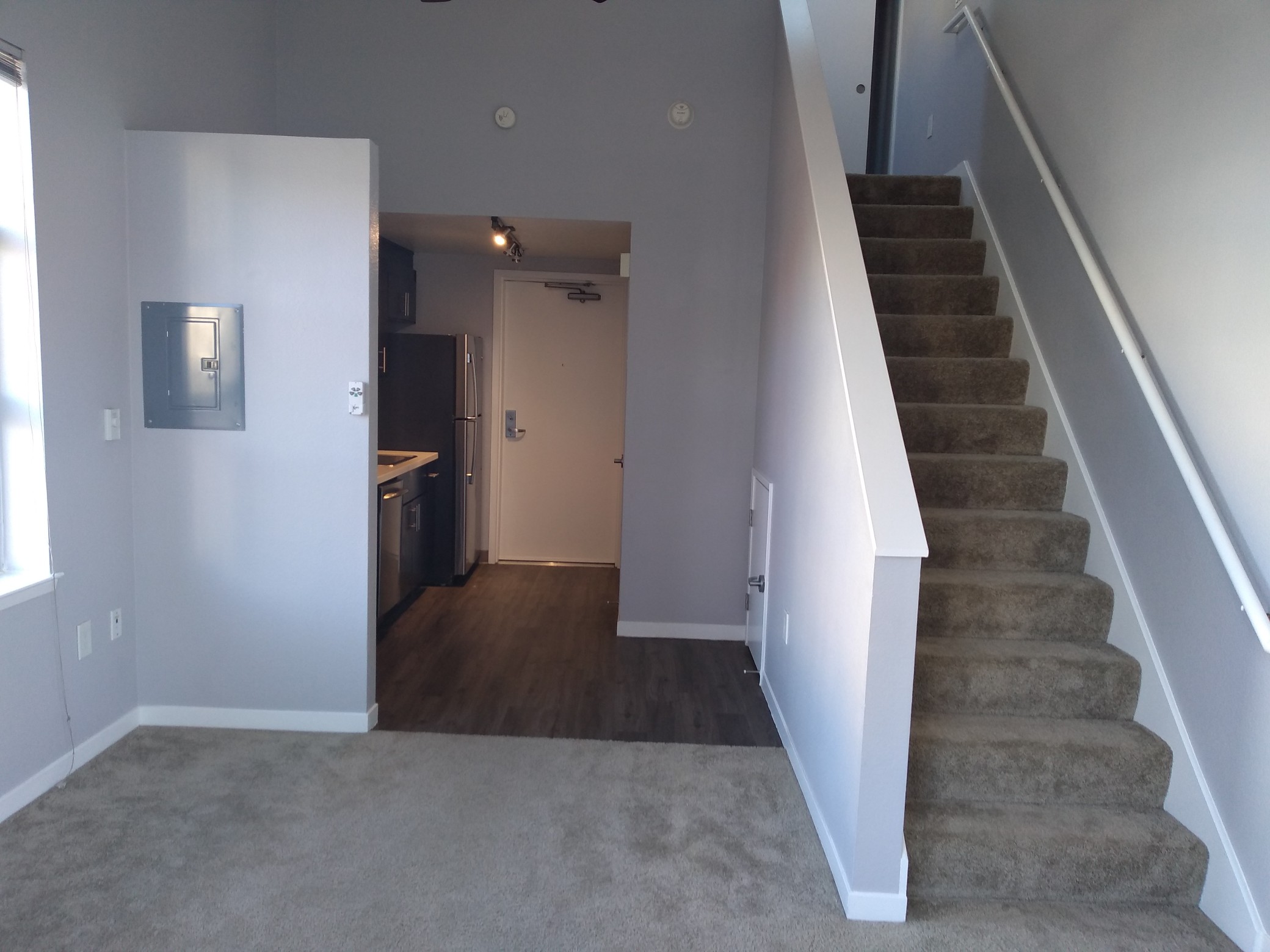View from the other side of the room, with a staircase up to a small loft and a small kitchen area.