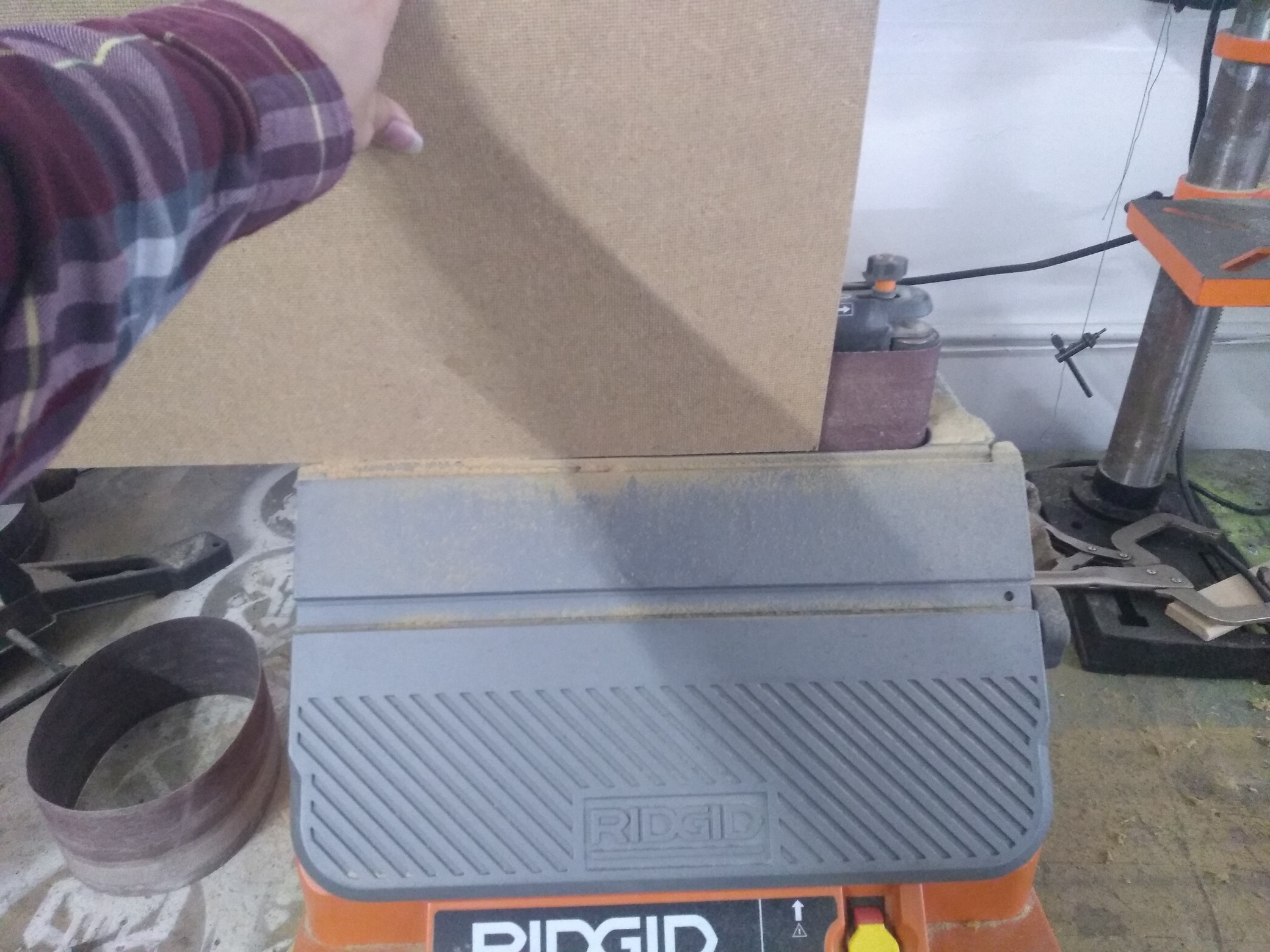 The piece of hardboard being held up against a belt sander.
