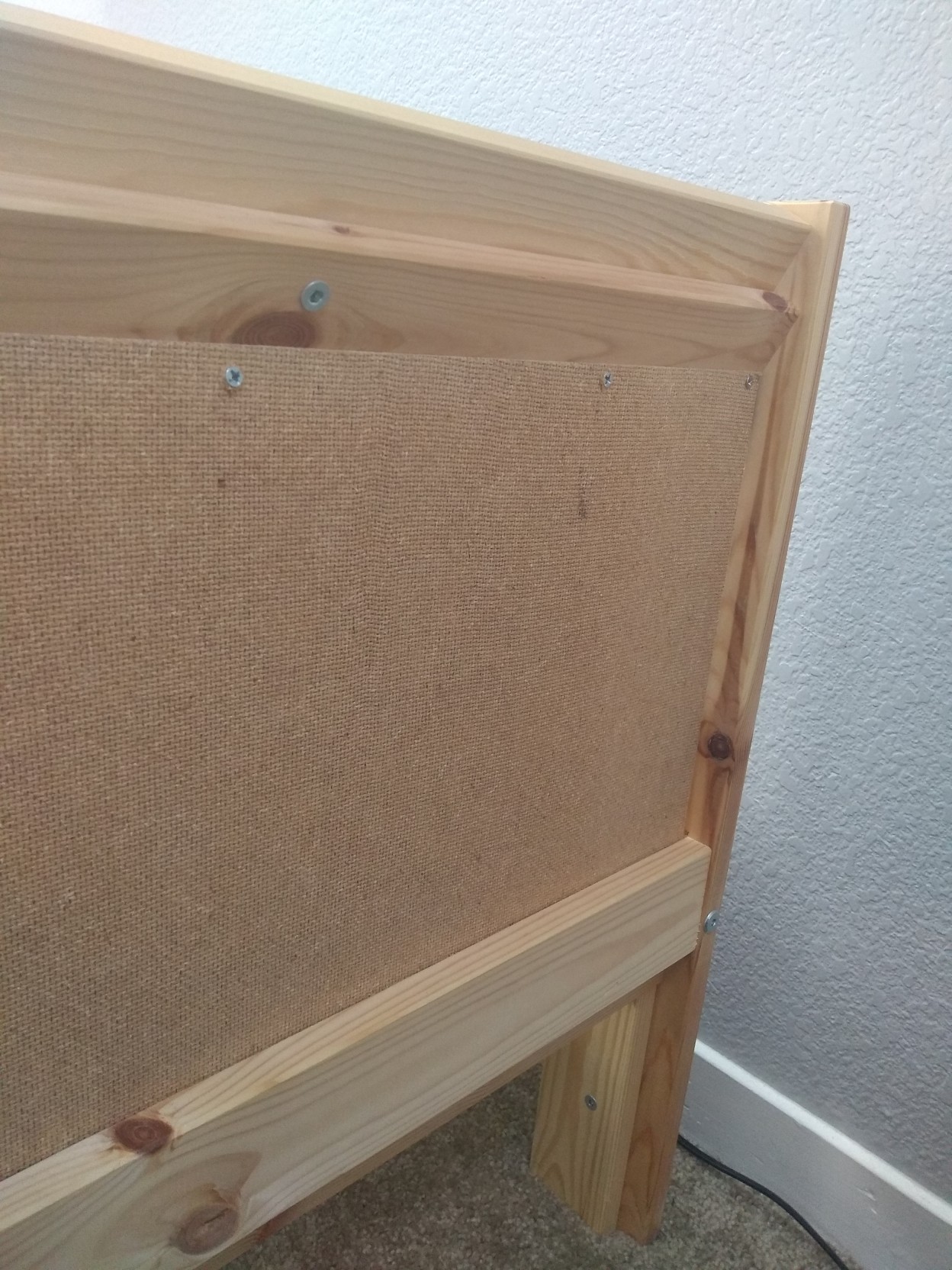 The back of a wooden bedframe, with some screws holding the board I made onto the headboard.