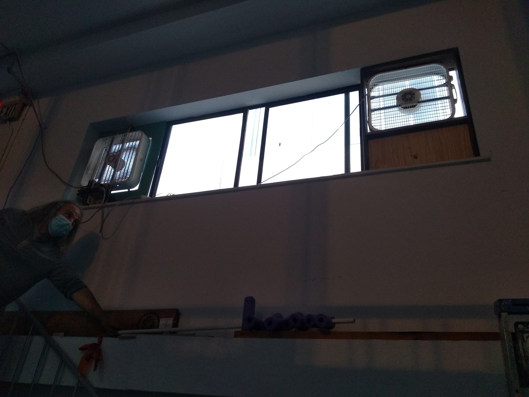 View up the stairwell, with two box fans in the window above the stairs. Dan leans in from the side to adjust something.